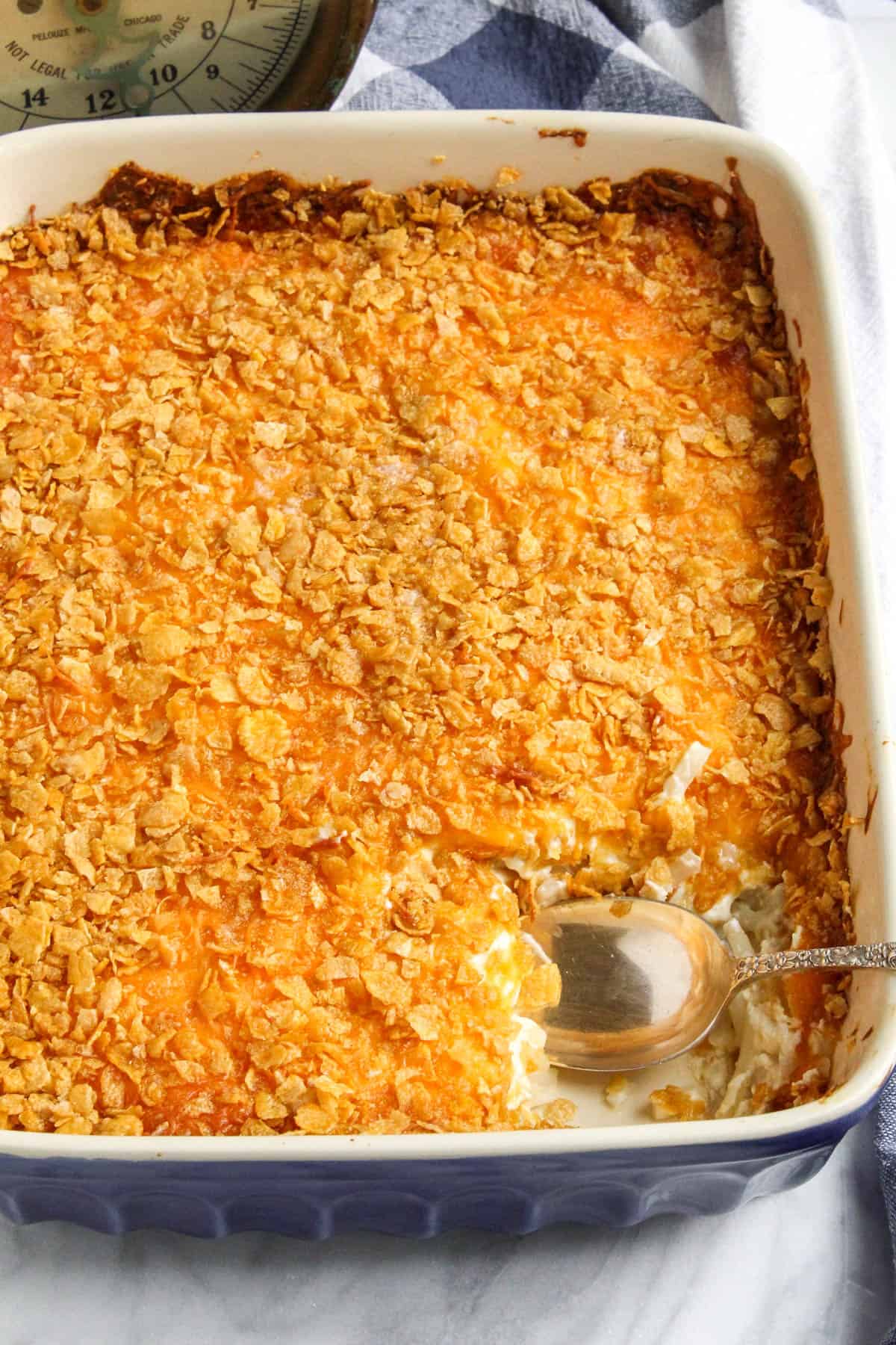 Cheesy potato casserole in baking dish with serving spoon.